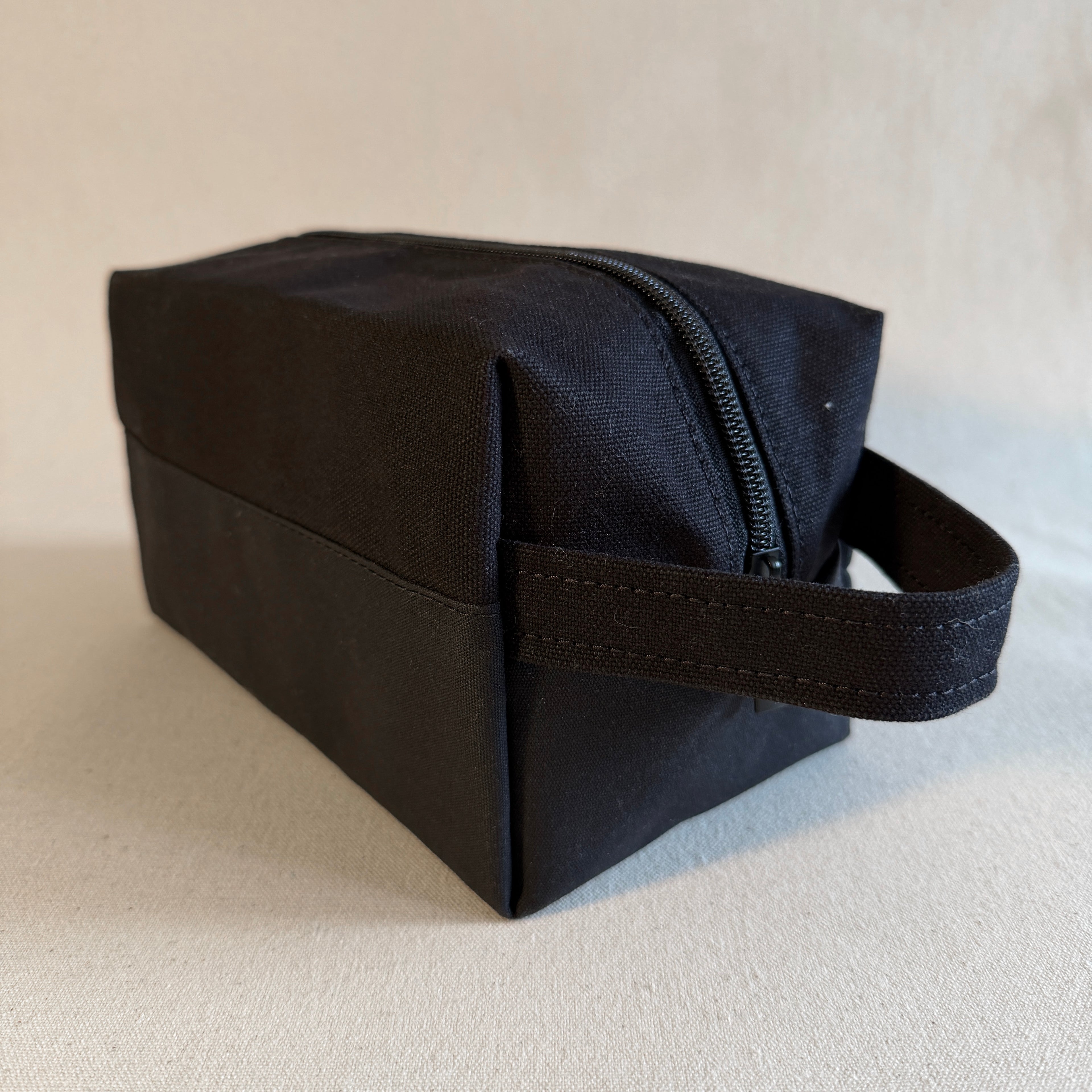 Black toiletry bag with a handle on a light beige background