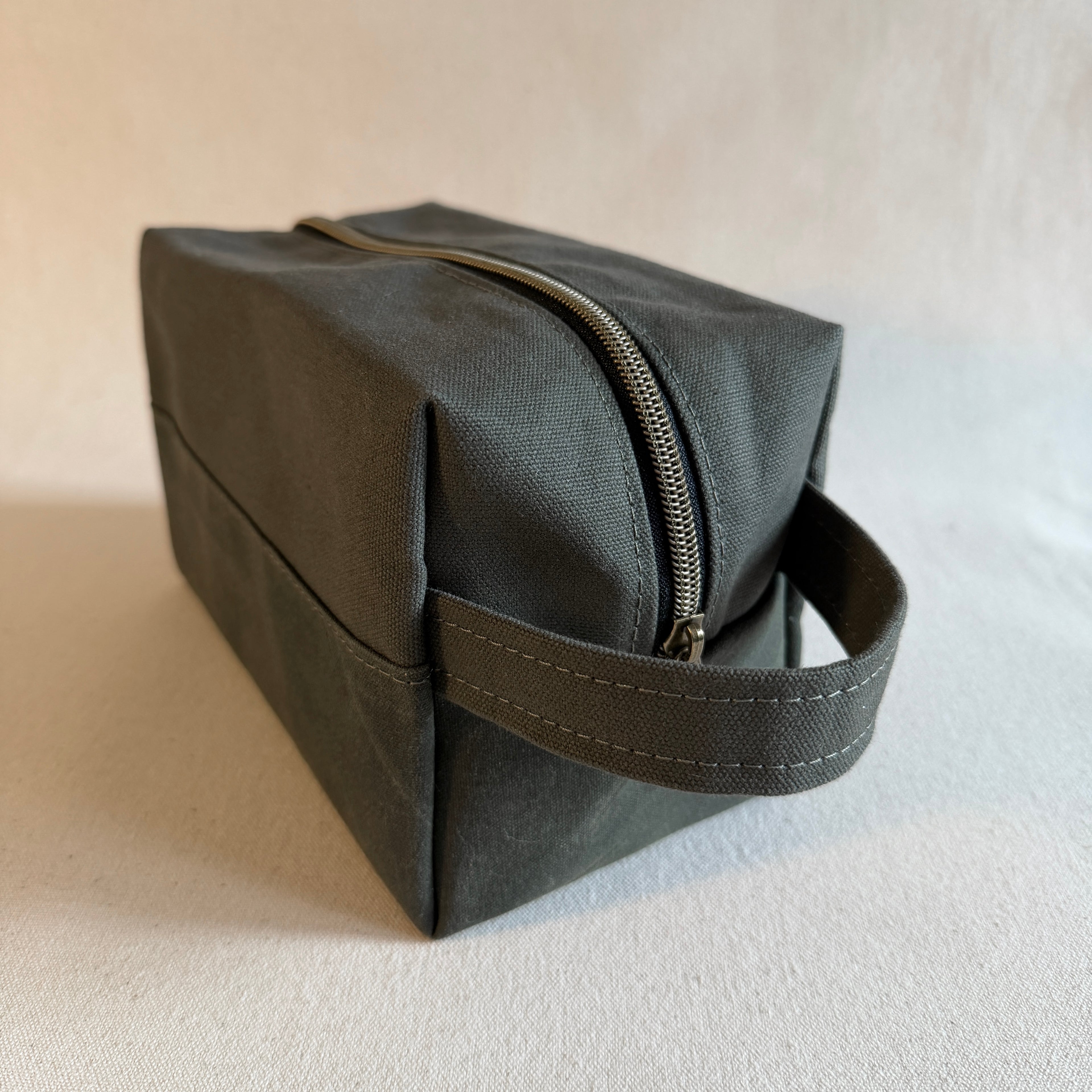 Dark olive green toiletry bag with a handle on a light background