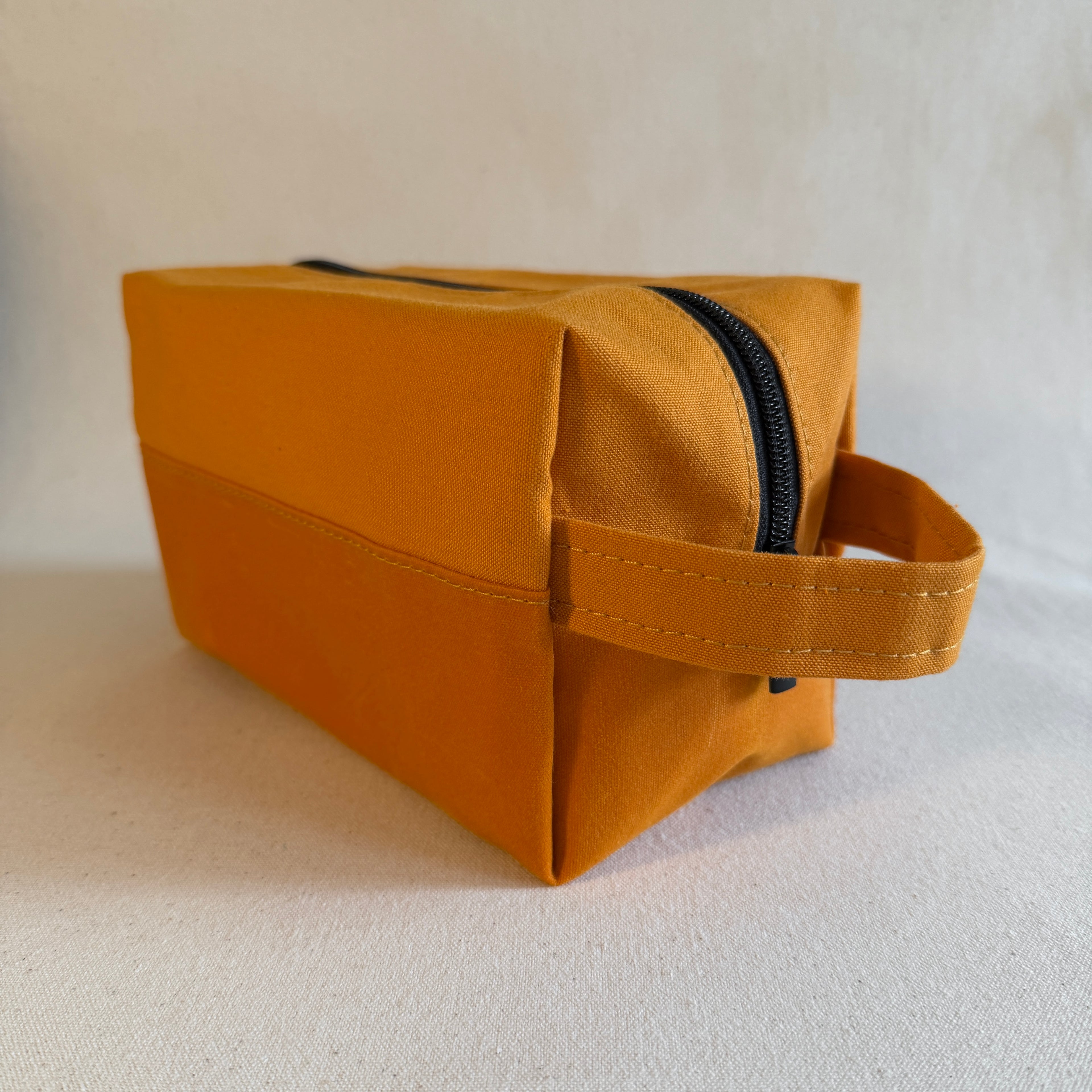 Yellow toiletry bag with a black zipper on a light background