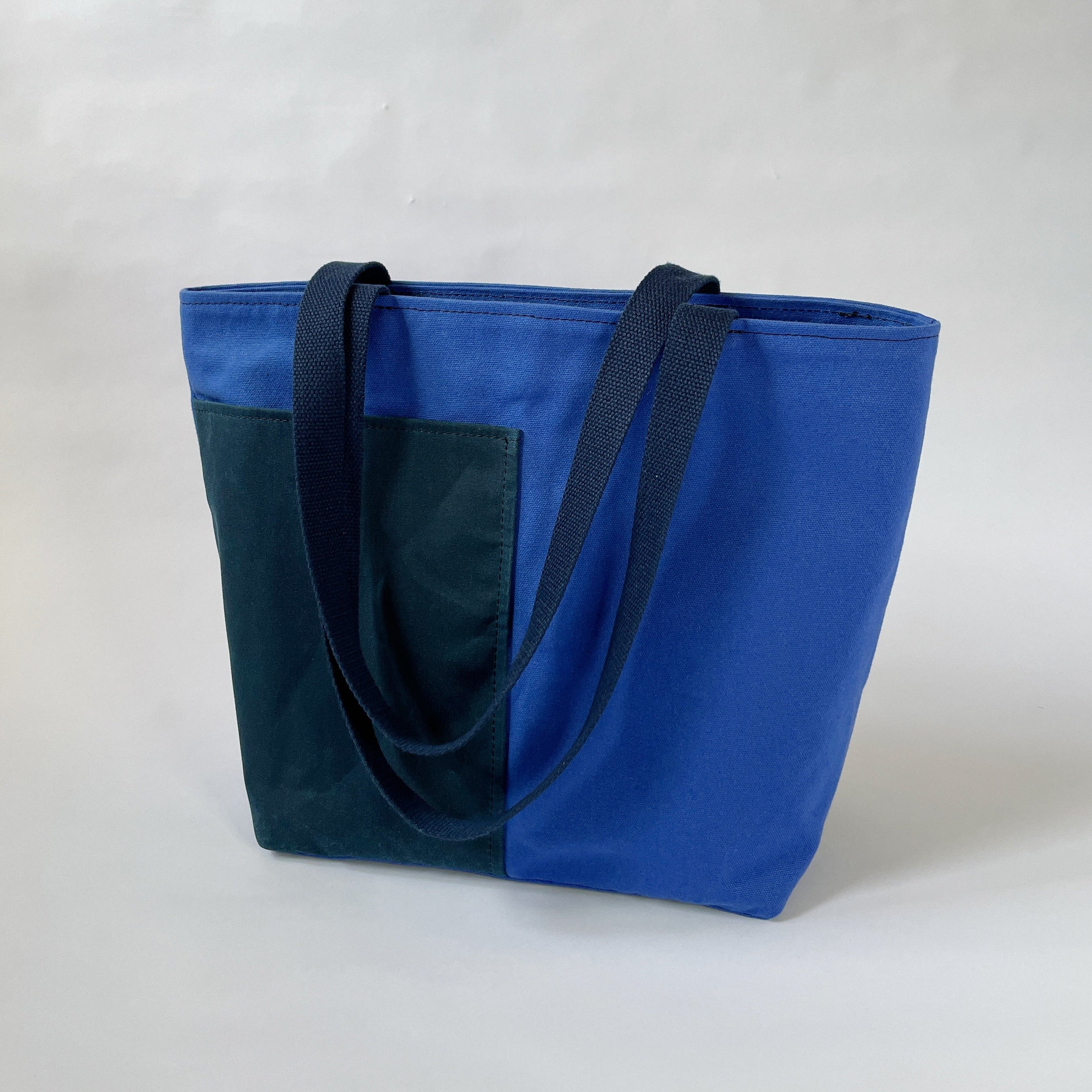 A blue and navy canvas tote bag with two handles, two lined exterior pockets, and two interior pockets, displayed against a neutral background.