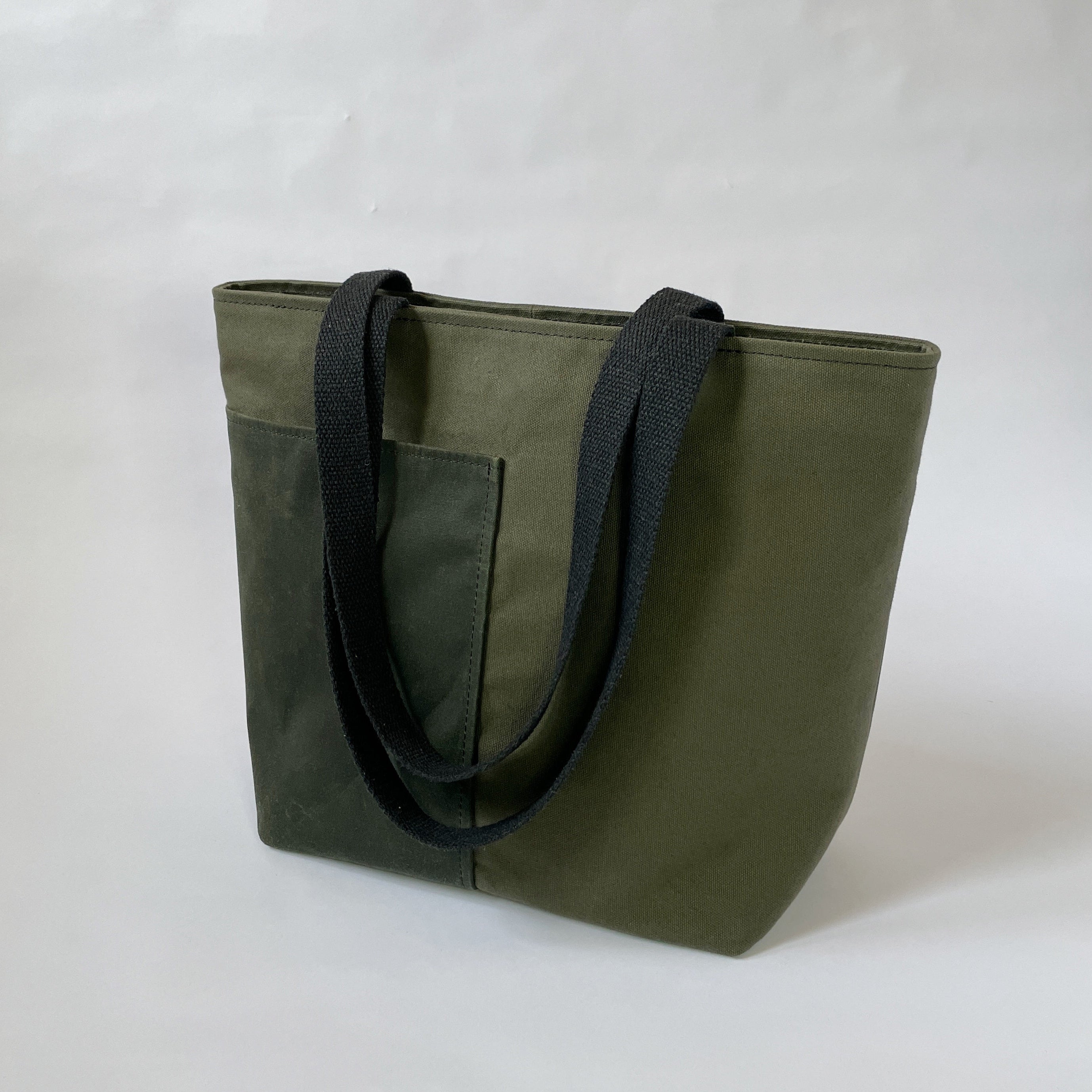 A dark olive canvas tote bag with two black handles, two lined exterior pockets, and two interior pockets, displayed against a neutral background.
