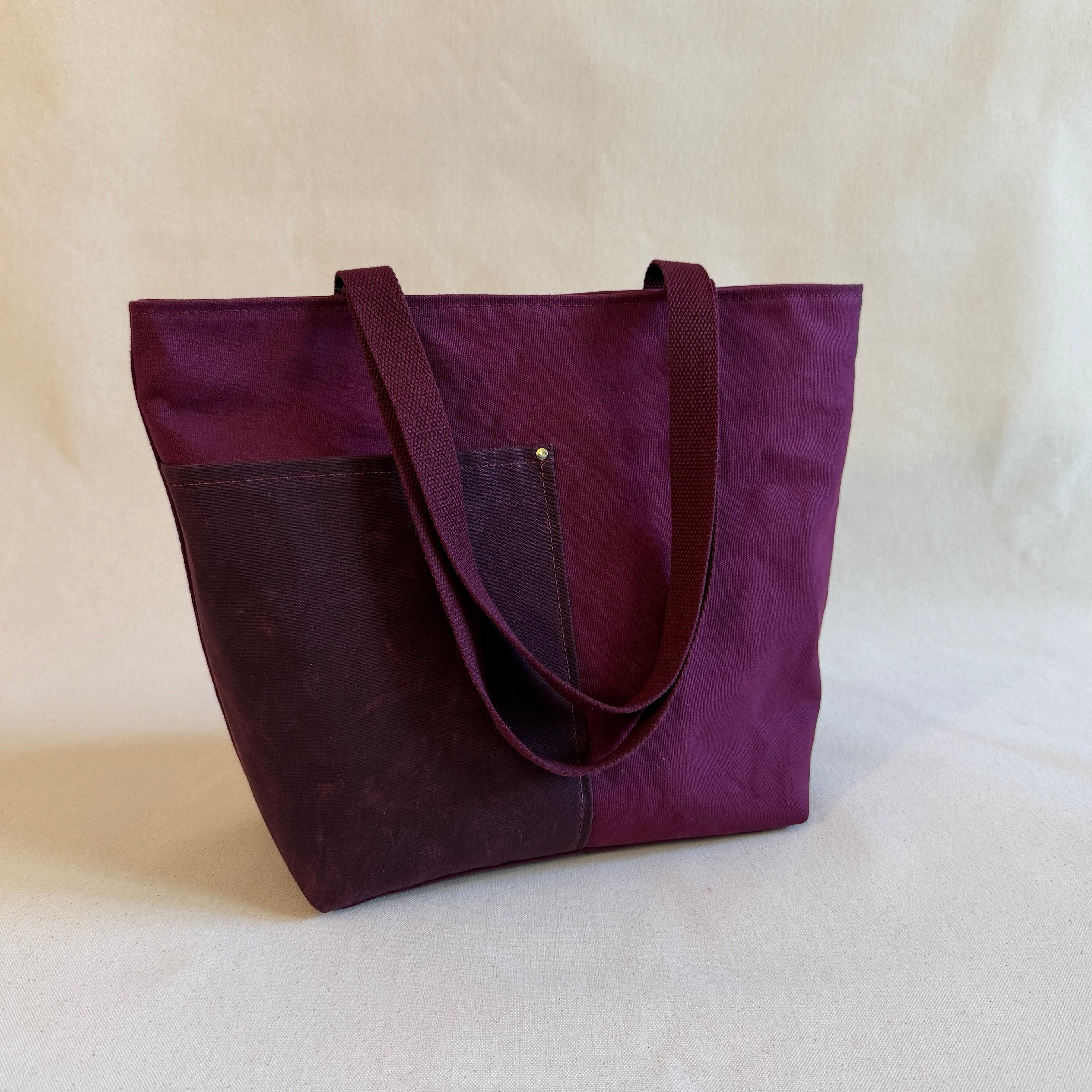 Maroon canvas tote with deep red pockets on a neutral background.