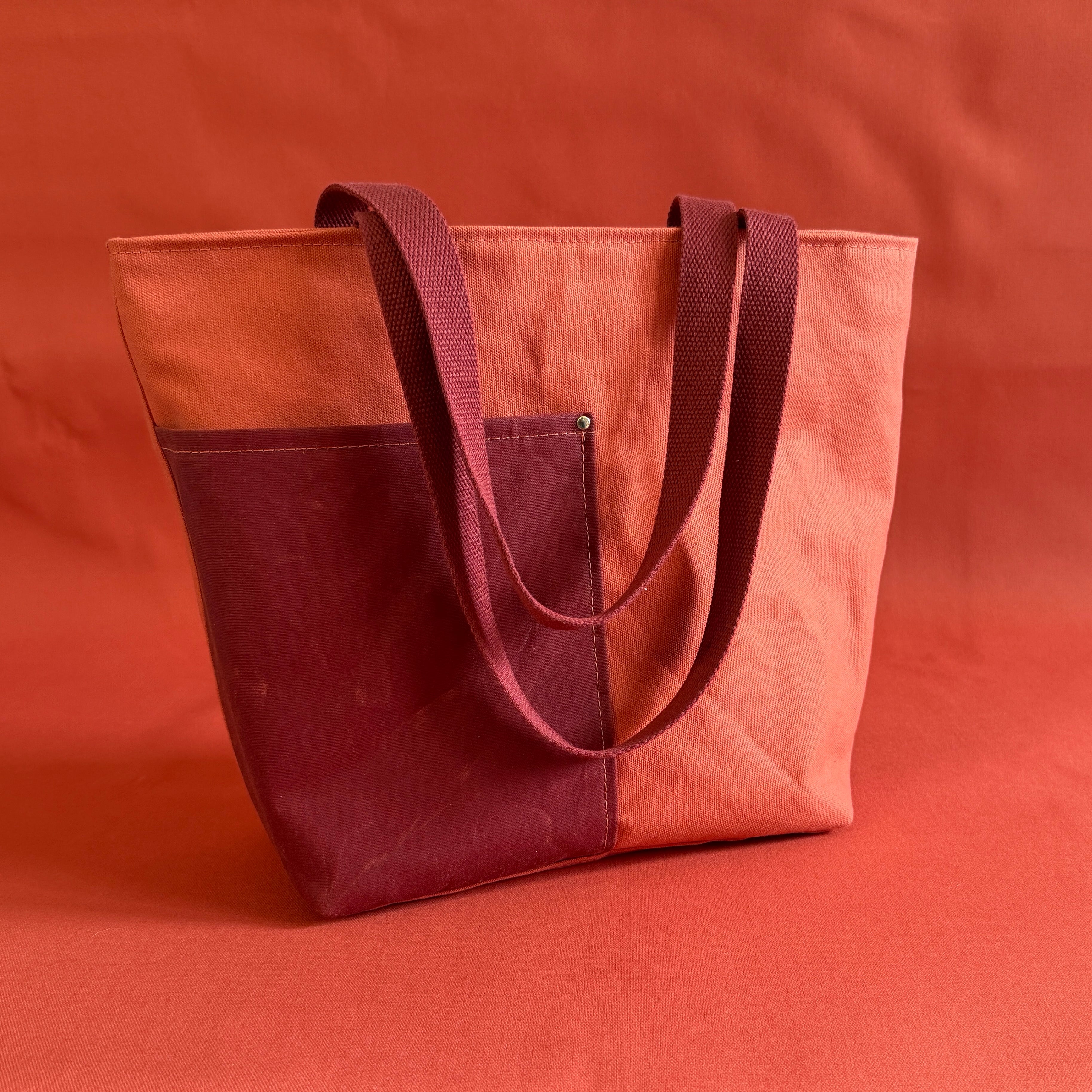 Two-toned tote bag with terra cotta and maroon colors on a matching background
