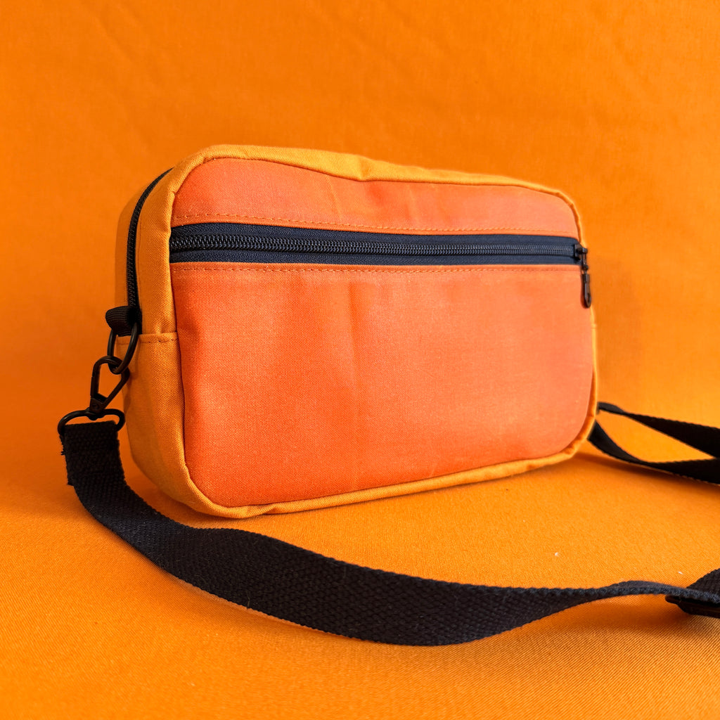 Orange and yellow bag with a black strap on an orange background