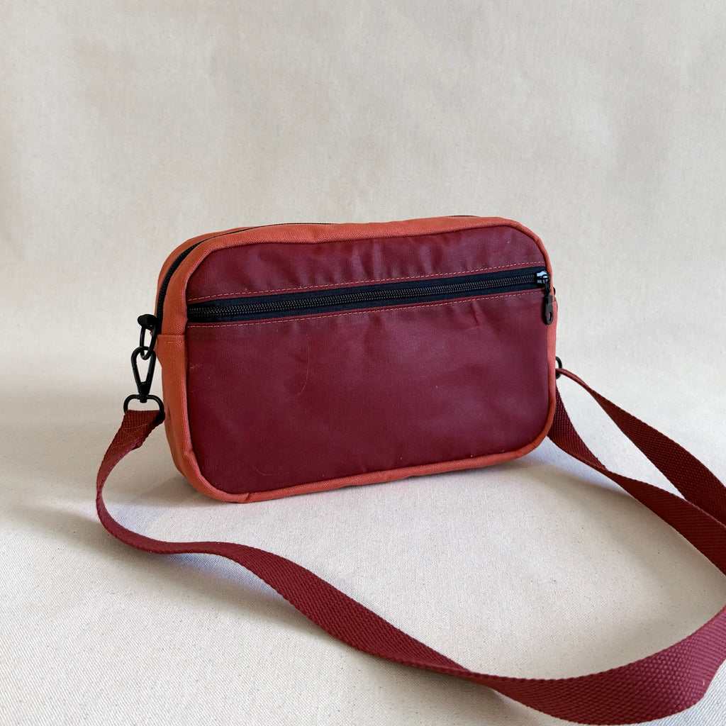 Pinkish-red crossbody bag with a strap on a beige background
